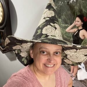 Handmade witch hat in black fabric with cream roses, worn by the maker